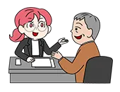 老齢の男性客にスーツの女性が書類を持ちながら説明をしている、ふたりはデスクを挟んで向かい合わせに座っている