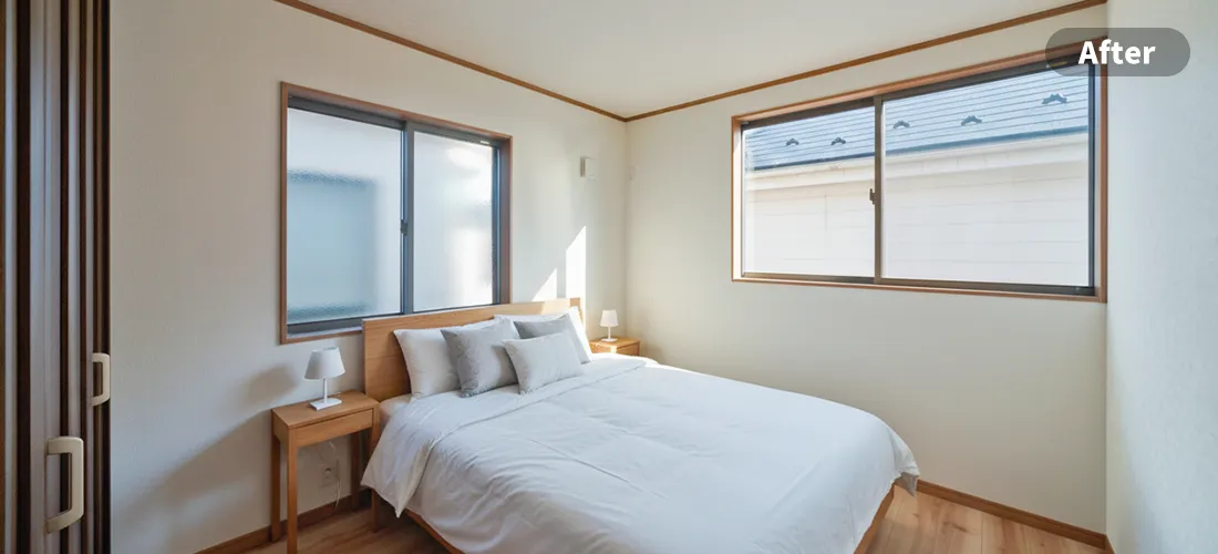 寝室のステージングアフター画像　壁にベッドの上の方が付く形でダブルベッドが置かれ、その横にサイドテーブルと小さなライトが配置されている